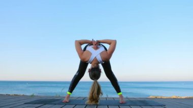 Güzel genç bir kadın mavi denize karşı deniz kenarında yoga egzersizleri yapıyor..
