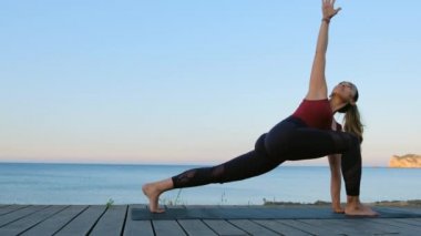 Güzel genç bayan deniz kenarında mavi denize karşı yoga egzersizleri yapıyor..