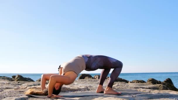 Young attractive woman practices yoga in wheel pose on the beach. — Stock Video