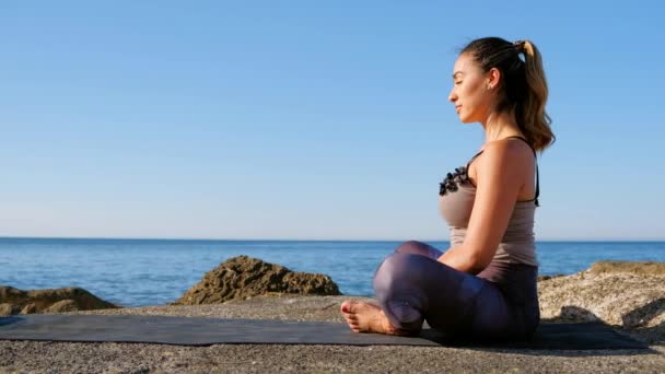 Nyugodt fiatal nő meditál a tengerparton egy gyönyörű kék tenger ellen. — Stock videók