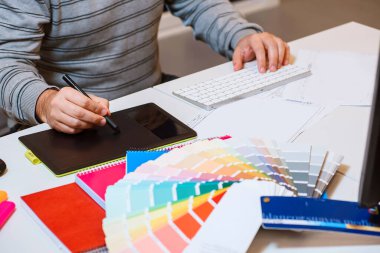 Ofisteki grafik tabletine erkek eli çizimi yakın plan. Taslaklar, renk paleti, işaretleyiciler ve klavye bir masada.