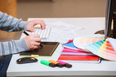 Ofisteki grafik tabletine erkek eli çizimi yakın plan. Üst Manzara. Taslaklar, renk paleti, işaretleyiciler ve klavye bir masada.