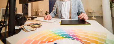 Fotoğrafçı-tasarımcı bir masada çalışıyor. Nehirde grafik tablet tutuyor.