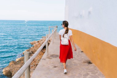 Uçurumun kenarında kırmızı bir elbise giymiş bir kadının İspanya 'daki kayalıklara bakışının arka görüntüsü..