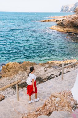 Sırtında sırt çantası olan güzel bir kızın dağ merdiveninden aşağı inen kırmızı deniz ve kayaların manzarası.