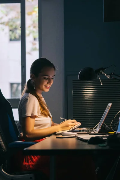 the girl works at the computer is focused on work in the office conceived in search of a new idea writes in a notebook