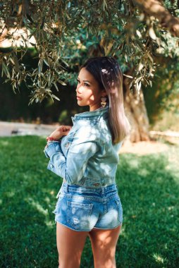 Kot ceketli zeytin ağacının yanında güzel bir sarışın ve açık mayo giymiş bir şort. Güzel bir portre ve yüzünde ışık