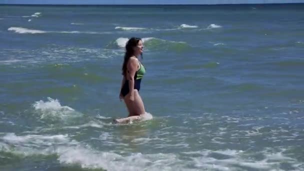 Hermosa morena caucásica chica en traje de baño con el pelo largo que va al agua en el mar pasando las olas — Vídeos de Stock