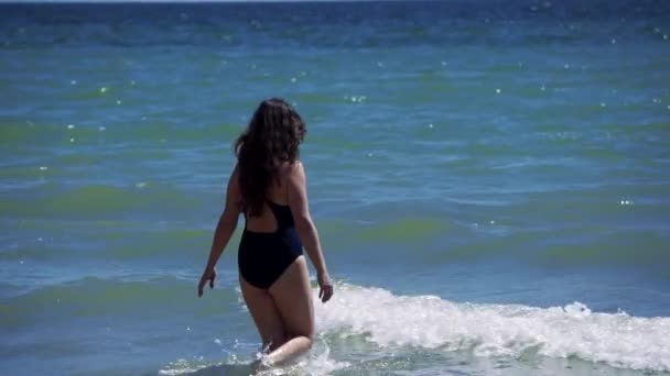 Bruna ragazza con i capelli lunghi andare in acqua in mare passando le onde — Video Stock