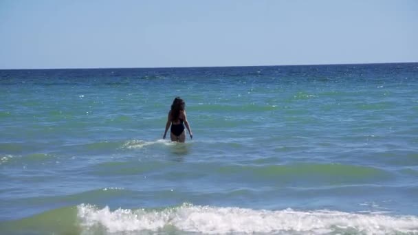 Dívka Bruneta s dlouhými vlasy vstoupí do vody na moři kolem vlny — Stock video