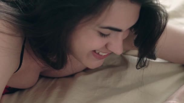 Девушка-брюнетка в нижнем белье лежит на кровати и болтает в онлайн-чате — стоковое видео