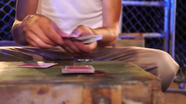Чоловік з шрамом на руці перемішує карти і віддає їх друзям, перш ніж грати на старій дерев'яній коробці — стокове відео