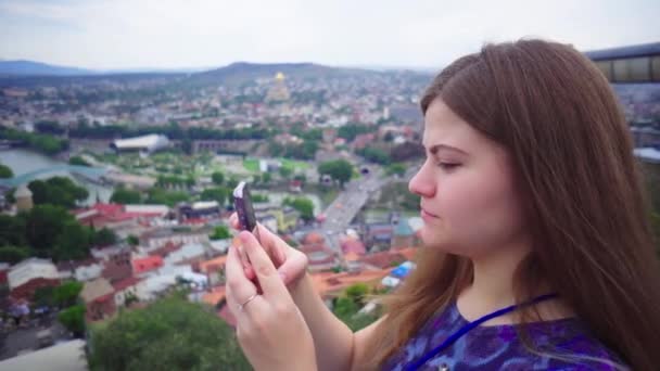 Young beautiful tourist girl is taking pictures of cityscape on smartphone camera and smiling — Stock Video