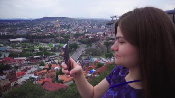 Menina jovem turista bonito está tirando fotos de paisagem urbana na câmera do smartphone sorrindo e olhando para a frente — Vídeo de Stock