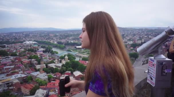 Chica joven turista mira en prismáticos en paisaje urbano hermoso fondo de vista en Tiflis — Vídeos de Stock