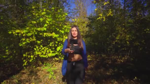 Brunette young woman blogger going in forest and recording video for vlog using camera — Stock Video