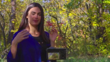 Blogger karizmatik genç kadın konuşmaya ve aktif el hareketi ve gülümseyen sonbahar orman kamerada yanında oturan yakın çekim