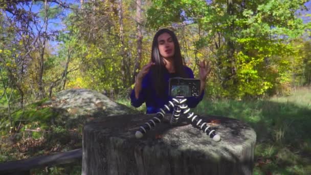 Young woman blogger sitting next to camera on the nature talking and showing thumbs up gesturing and smiling slow motion — Stock Video