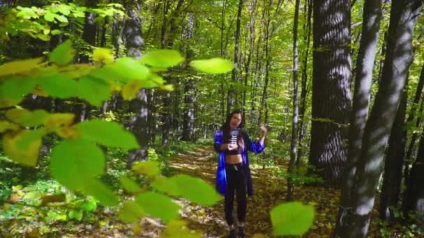 Брюнетка блоггер идет в осенний лес и записывает видео для видеоблога с помощью камеры — стоковое видео