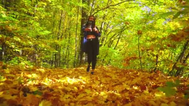 Zeitlupe Bloggerin charismatische junge Frau läuft im Herbst Wald und nimmt Video für Vlog mit Kamera sprechen und zeigt Daumen nach oben — Stockvideo