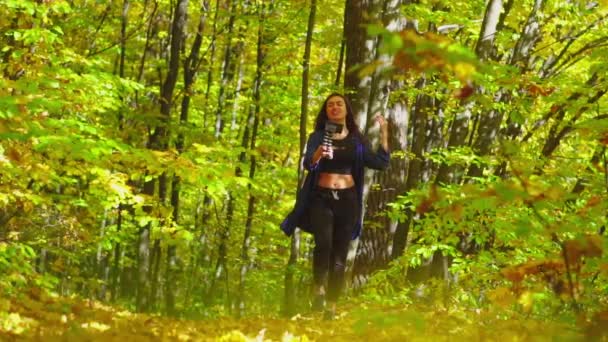 Blogging charismatic young woman is walking in sunny autumn forest and recording video for vlog using camera slow motion — Stock Video