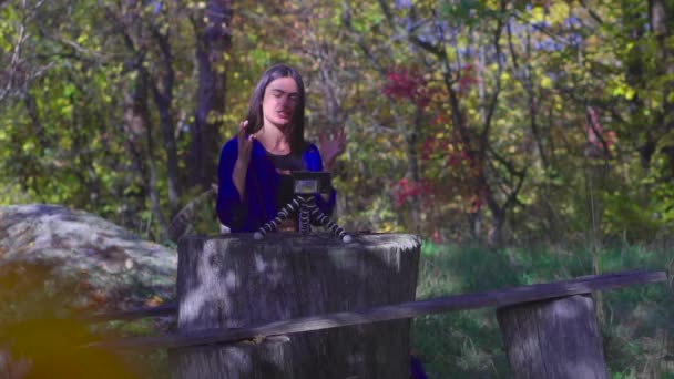 Заметьте харизматичную молодую женщину, сидящую рядом с камерой, показывающую большие пальцы и улыбающуюся в осеннем лесу, говорящую и жестикулирующую замедленной съемкой — стоковое видео