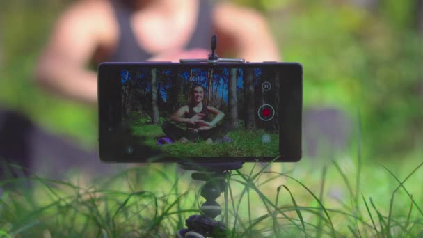 Jovem morena mulher vlogger tiro treino processo de vídeo para seu blog em um parque com smartphone — Vídeo de Stock