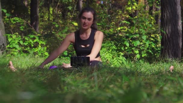 Schöne junge brünette Frau schießt Workout-Prozess-Video für ihren Blog in einem Park mit Smartphone — Stockvideo