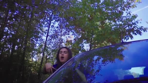 Молодая брюнетка, высунувшись из окна машины, делает селфи с телефоном — стоковое видео