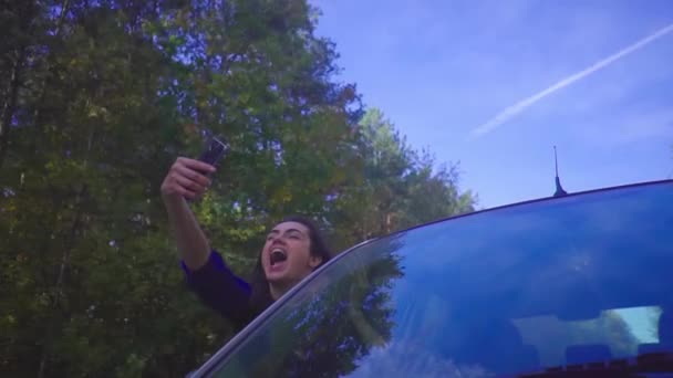 Νέοι μελαχρινή γυναίκα ευτυχισμένη κλίνει έξω από το παράθυρο και κάνει selfie με το τηλέφωνο στο αυτοκίνητο κατά την οδήγηση μέσα από δάσος αργή κίνηση — Αρχείο Βίντεο