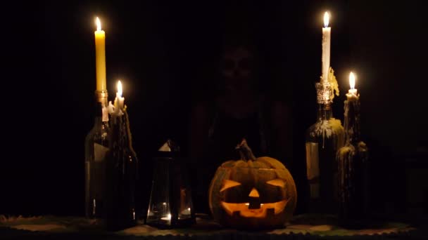 Halloween-Hexe leckt Messerklinge in Ketten mit Totenkopf-Make-up Zauberkürbis und Kerzen — Stockvideo