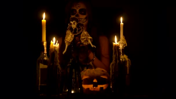 Halloween sorcière avec le maquillage du crâne rend vaudou tient couteau et sortilège magique chaînes de citrouille et bougies — Video