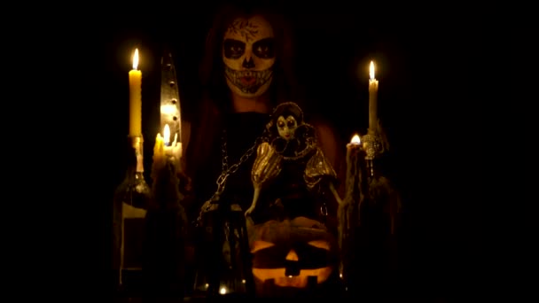 Halloween boszorkány a koponya smink teszi a voodoo tart kés és a varázslat, mágia sütőtök láncok és a gyertya wispering — Stock videók
