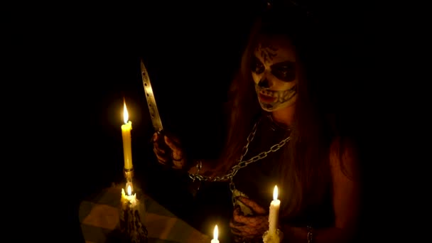 Bruja de Halloween con maquillaje de cráneo sostiene cuchillo y hechizo sabelotodo cadenas de calabaza mágica y velas — Vídeos de Stock