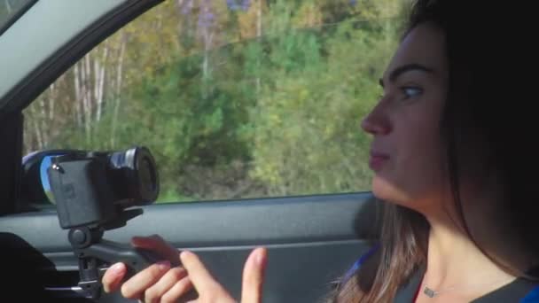 Linda jovem morena em um carro filmando vídeo para seu blog com câmera — Vídeo de Stock