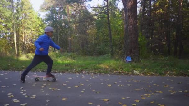 Ребёнок на скейтборде катается на коньках под открытым небом в осеннем парке — стоковое видео