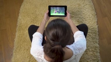 Kadın evde halı üzerinde otururken spor eğitim ekranda izlemek için Tablet PC'yi kullanma