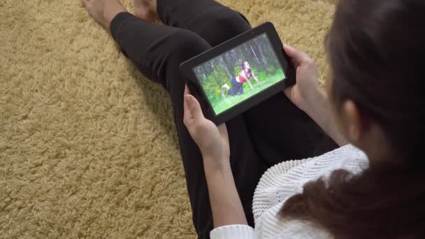 Chica viendo video de entrenamiento deportivo utilizando la pantalla de la tableta PC mientras está sentado en casa en la alfombra — Vídeo de stock