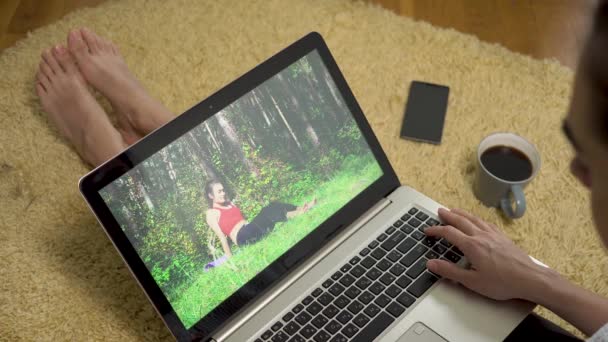 Jonge vrouw kijken naar sport opleidingsvideo met behulp van laptop scherm zittend thuis op het tapijt — Stockvideo