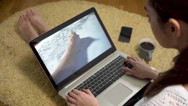 Γυναίκα ψάχνει στο lap-top με τέχνη σκίτσου βίντεο στην οθόνη ενώ κάθεται στο σπίτι στο χαλί — Αρχείο Βίντεο