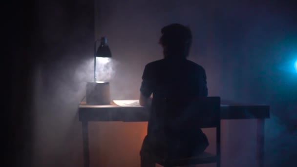 Artista homem sentado à mesa com papel e esboço padrão em estúdio de arte escura com fumaça mística e olhando para o lado — Vídeo de Stock