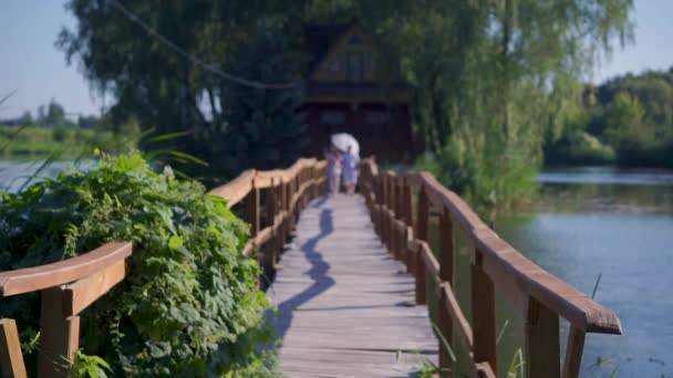 Man och kvinna i kärlek i kärlek gå på en trä land bro med ett vitt paraply i sommardag — Stockvideo