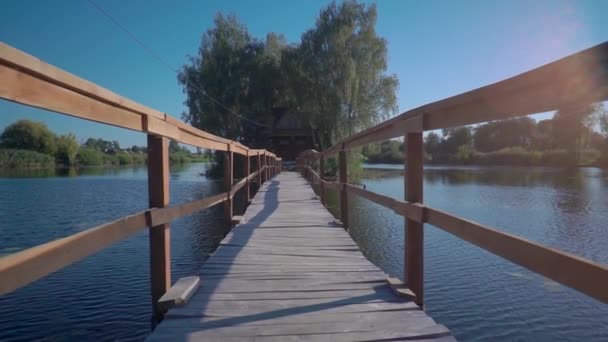 Puente de madera alargado que conduce a una cabaña de madera a través del río en un día soleado — Vídeos de Stock