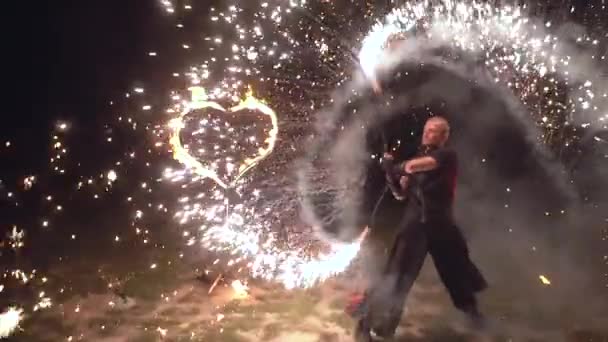 Spectacle de feu homme artiste tordre des objets de feu dans ses mains avec le coeur brûlant sur le fond — Video