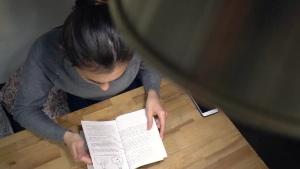Молодая брюнетка читает книгу в рамках подготовки к экзаменам — стоковое видео