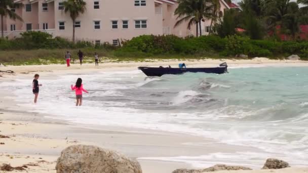 Feeport, Grand Bahama-12 maart 2019: kinderen spelen met de golven en de boot is wuivende op de golven — Stockvideo