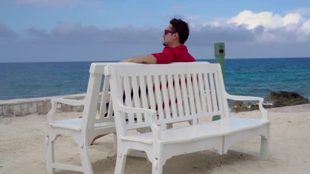 Hombre con anteojos sentado en el banco, mirando el océano y el humo — Vídeos de Stock