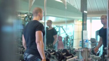 Spor salonunda ayna yansıtan dambıllarla antrenman yapan genç bir sporcu.