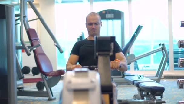 Oung sportsman makes an exercise on rowing simulator — Stock Video