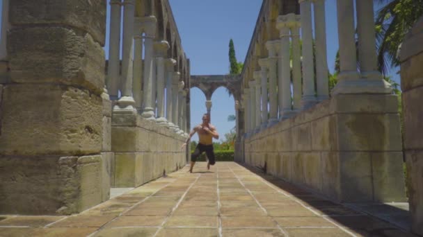 Sportsman makes squats with the movement among the ancient columns — Stock Video